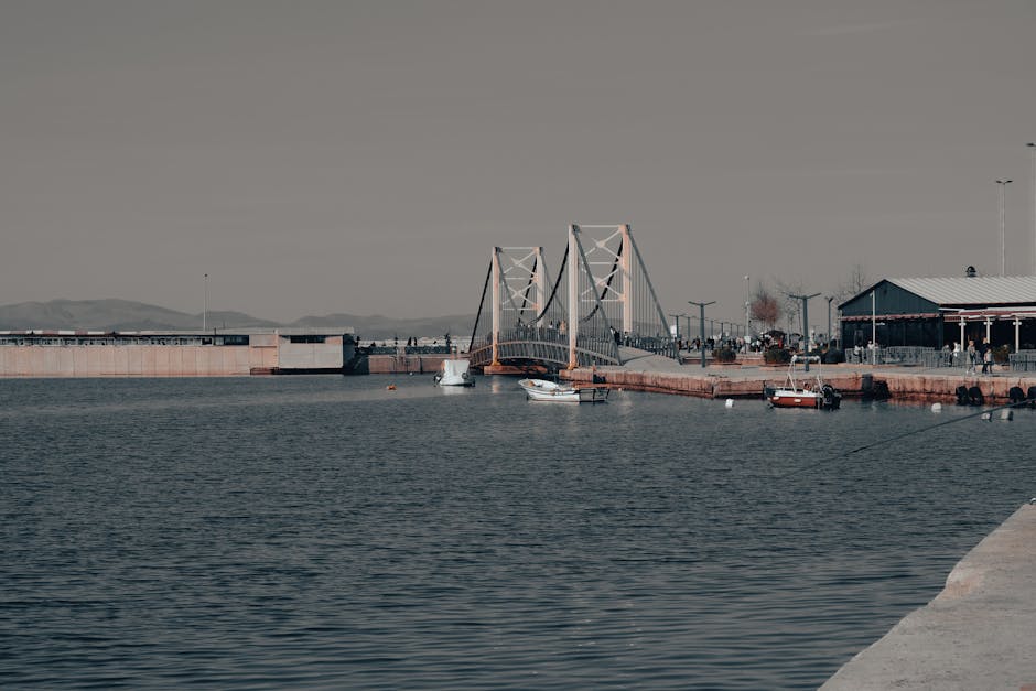 A peaceful scene of a suspension bridge over water, with boats nearby on a calm day.