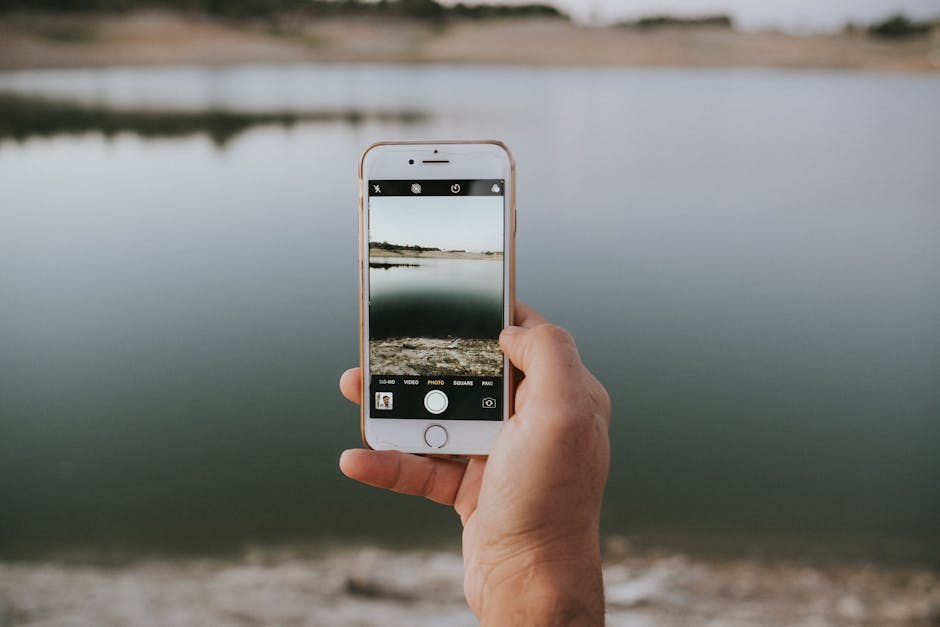 A close-up of a hand holding a smartphone capturing a serene lake view.