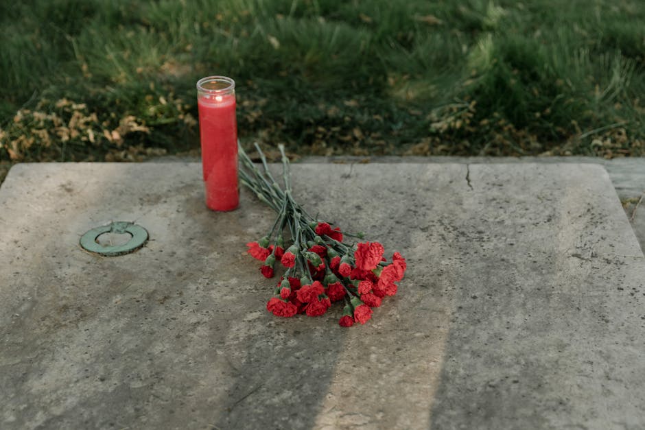 A solemn image of red carnations and a candle on a stone grave, symbolizing remembrance.