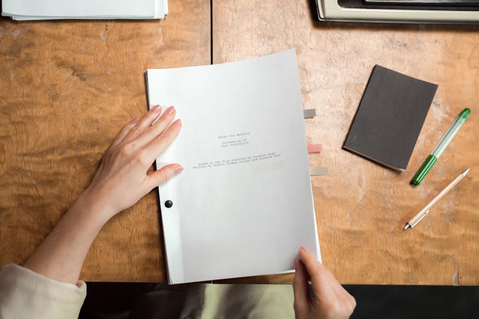 Close-up of hands organizing documents on a wooden desk with pen and notebook.