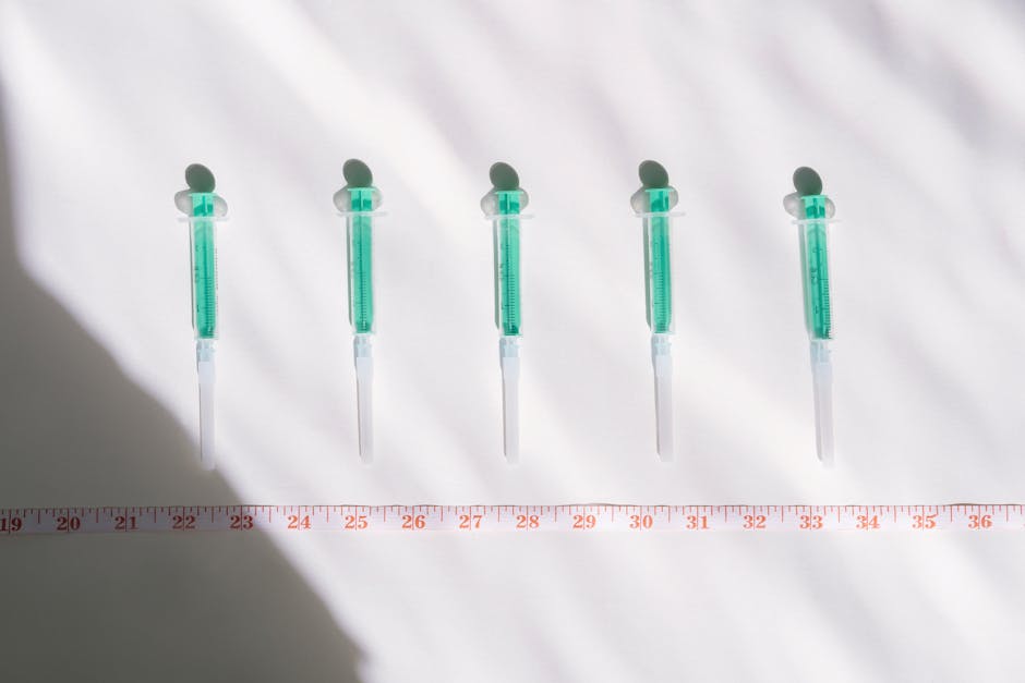 Top view of sterile syringes aligned with a centimeter ruler under bright light, casting shadows.