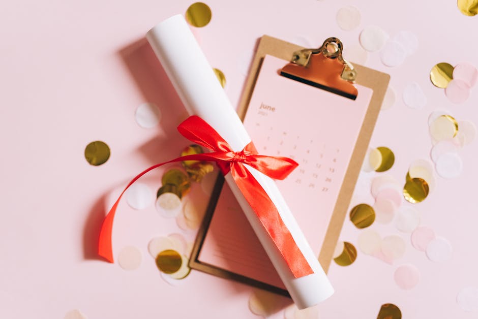 Flat lay of a graduation diploma with a red ribbon on a clipboard with confetti.