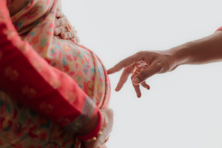 A close-up of a pregnant woman in traditional Indian attire with a hand gently reaching towards her belly.