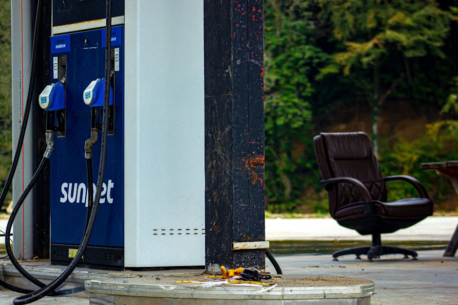 An outdoor gas station pump with a vintage look alongside an office chair, in a rustic setting.