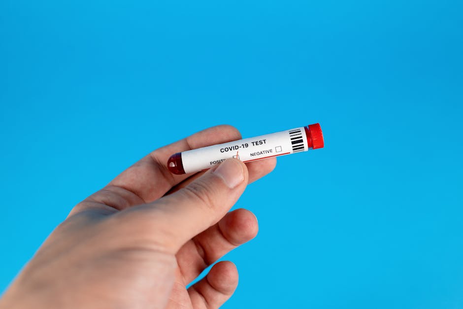 A hand holding a COVID-19 test tube against a blue background.