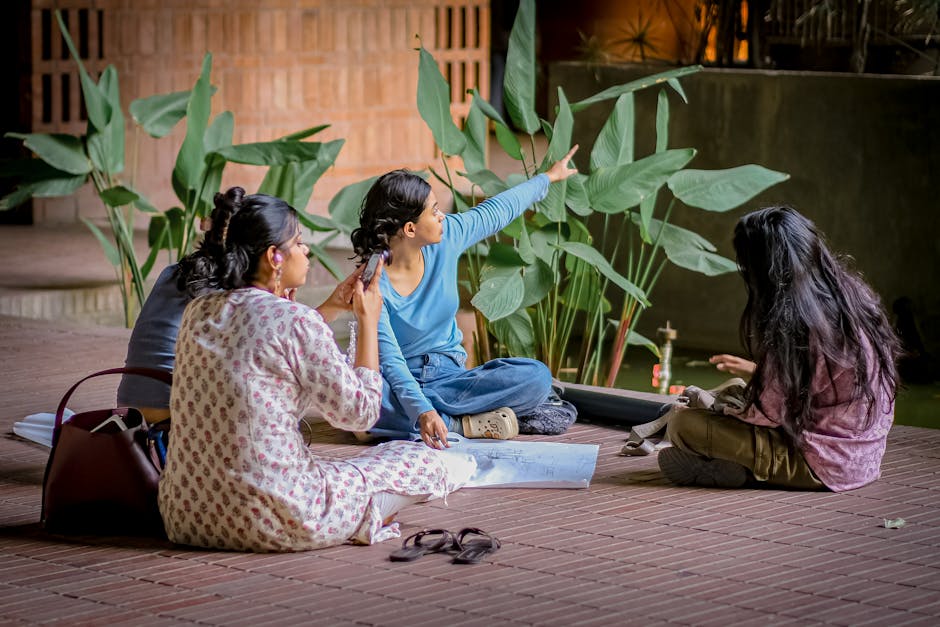 Three women engage in discussion while sitting on a brick patio surrounded by greenery.