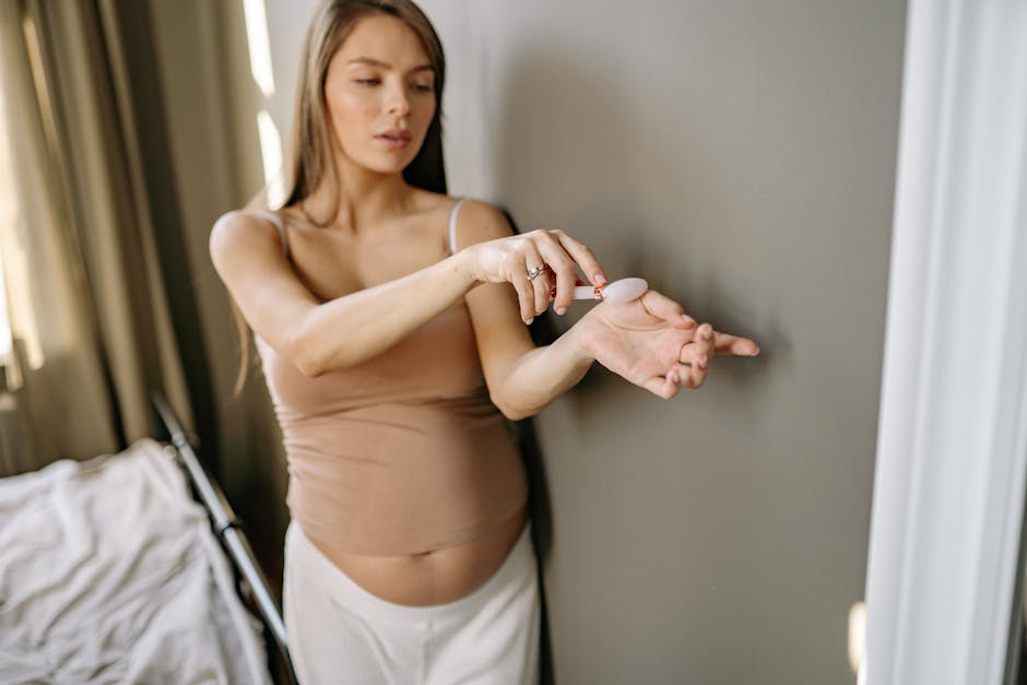 Pregnant woman in bedroom using a jade roller for self-care. Emphasizes wellness and relaxation.