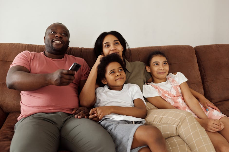 A family of four enjoying quality time together on the sofa, watching TV with smiling faces.