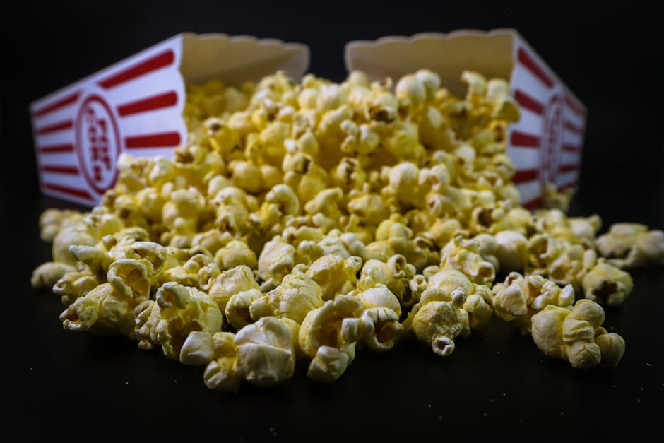 Delicious buttery popcorn spilled from a classic striped box on a dark background.