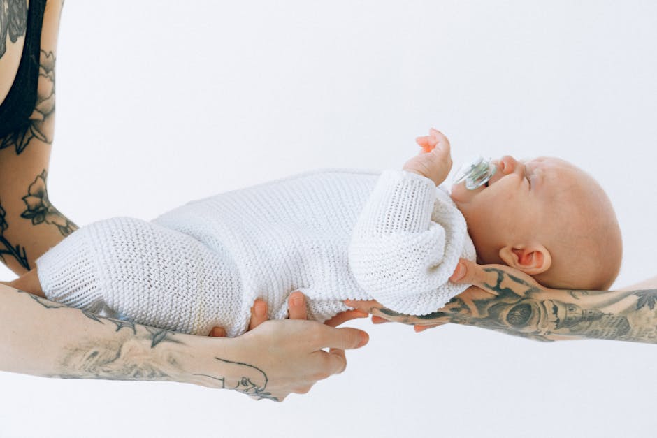 Tattooed arms cradle a peacefully sleeping baby, embodying modern parenthood's tender love.