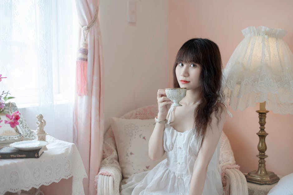 Woman enjoying a peaceful morning tea by the window in a cozy, pastel-toned room.