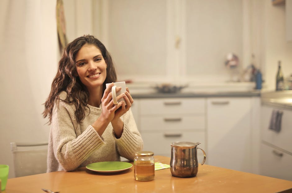 Woman smiling while holding a cup of tea in a cozy kitchen setting.