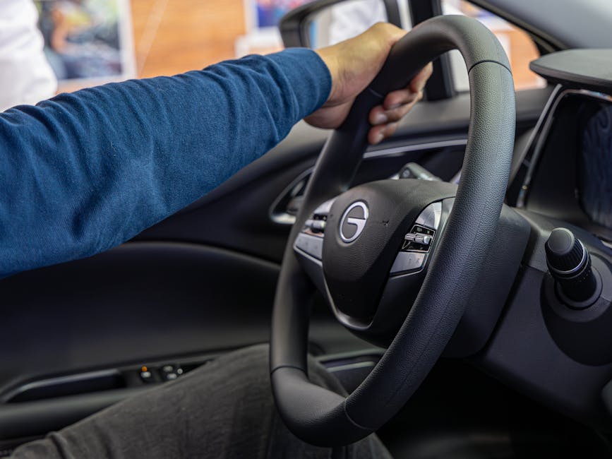 A person steers a car, focusing on a hand holding the steering wheel inside a vehicle.