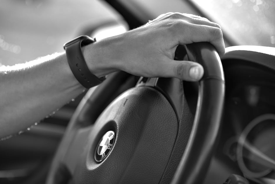 Black and white close-up of a hand gripping a BMW steering wheel, showcasing driving control.
