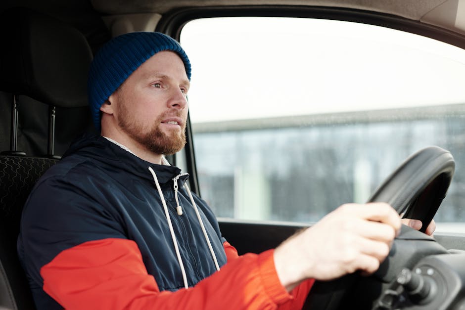 A bearded man wearing a hoodie and knitted cap driving a car, focused and attentive.