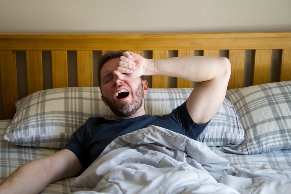 Man yawning and waking up in bed, starting a new day with the morning light.