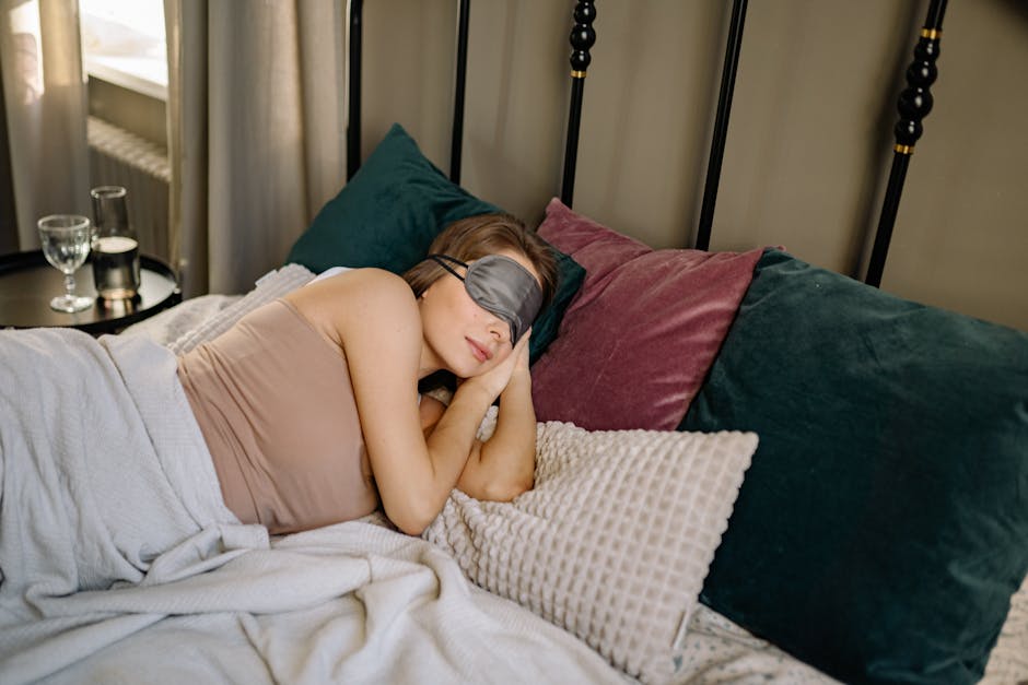 Woman resting peacefully in bed with a sleep mask, surrounded by cozy pillows in an inviting bedroom ambience.