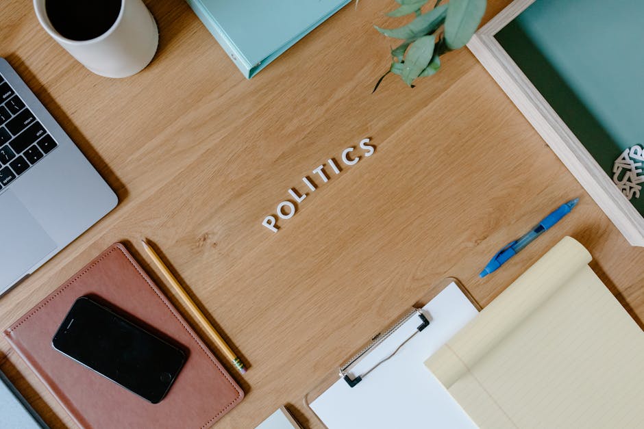 Overhead shot of a workspace with a politics theme, featuring a laptop, planner, and clipboard.