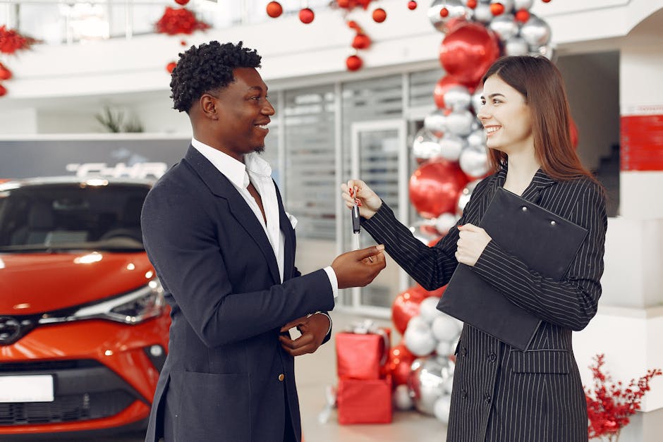 Side view of happy positive female dealer in formal classy wear passing car keys to  excited African American customer in trendy suit in car showroom