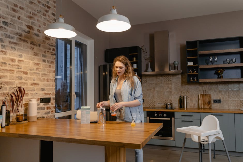 A woman making baby formula in a cozy kitchen with a high chair nearby.