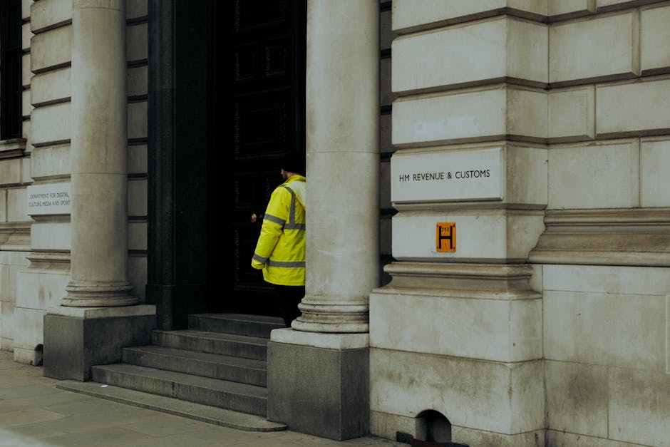 A guard in yellow jacket at the entrance of HM Revenue & Customs building in the UK.
