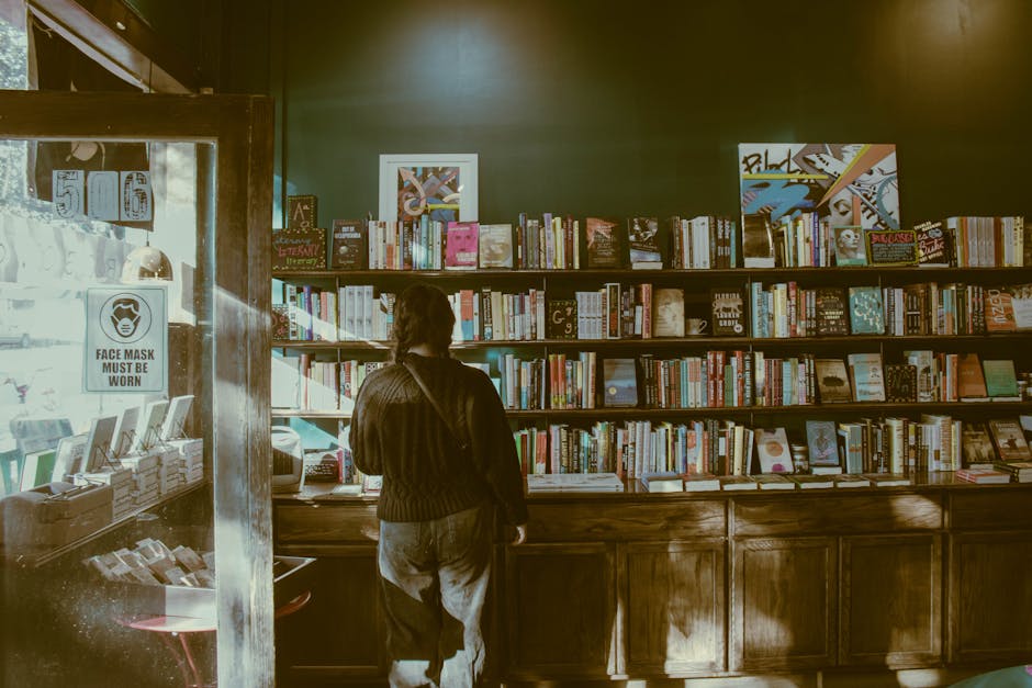 A person standing indoors, browsing books in a cozy bookstore with wooden shelves.
