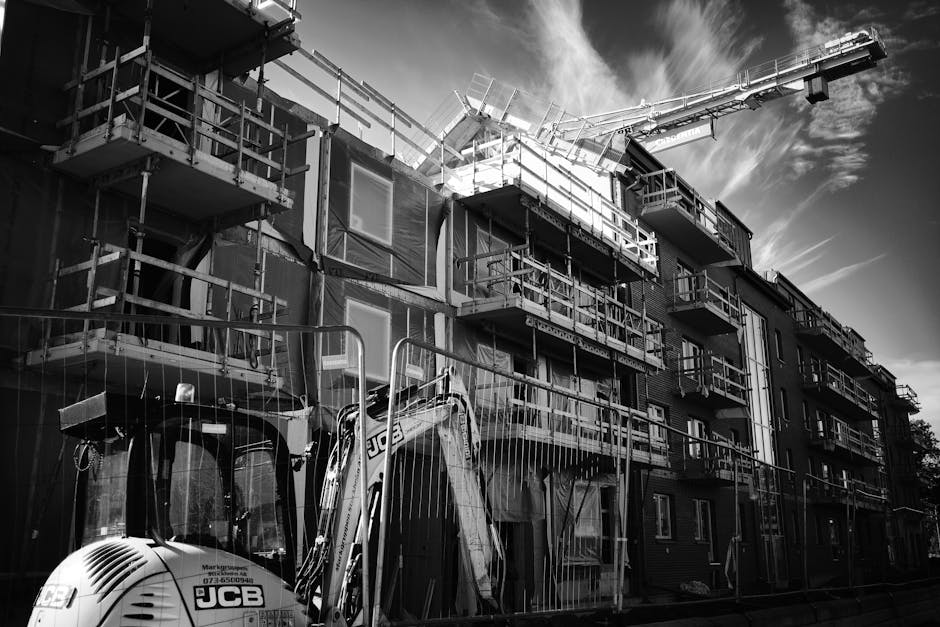 Monochrome image of a building under construction with a crane and scaffolding.