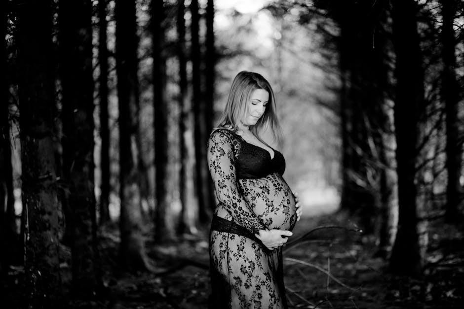 Anticipating mother in lace attire poses elegantly in a forest setting.
