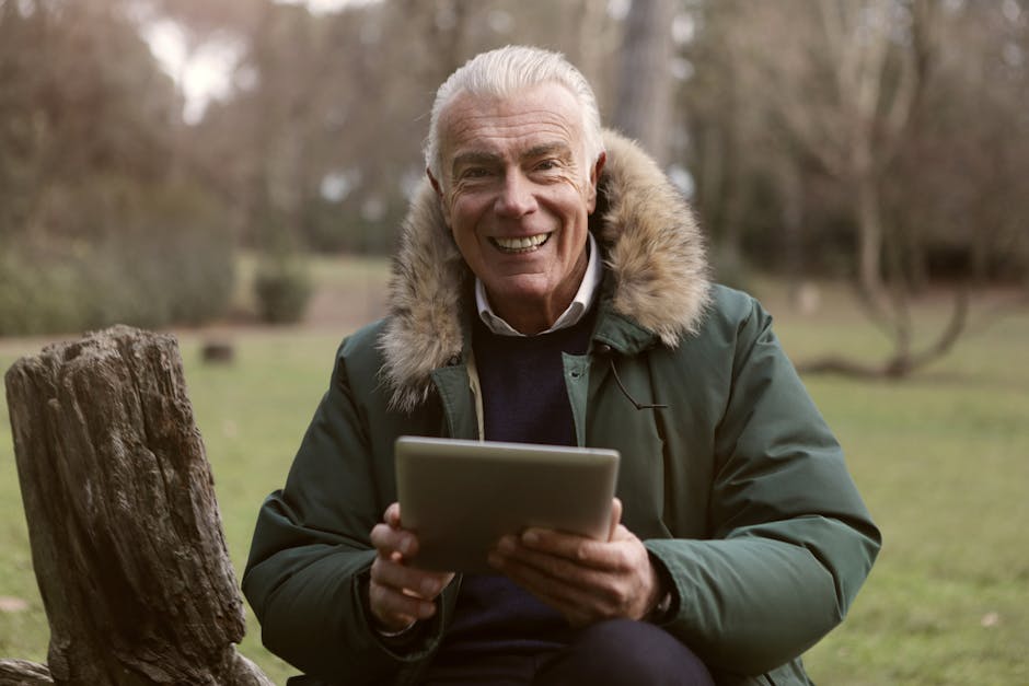 Happy elderly man using a tablet outdoors in a park setting.
