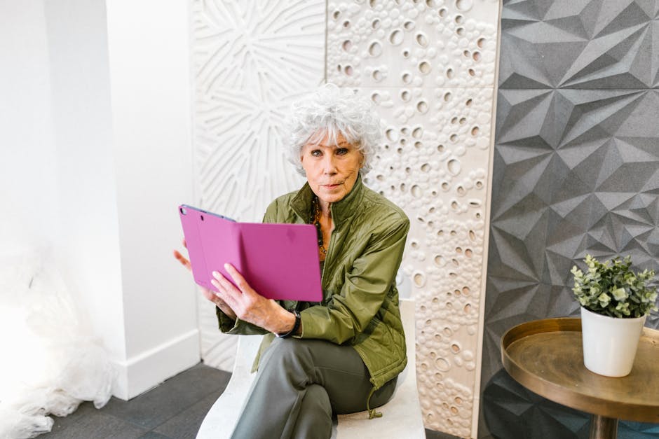 Elderly woman in a green jacket using a tablet in a stylish indoor setting.