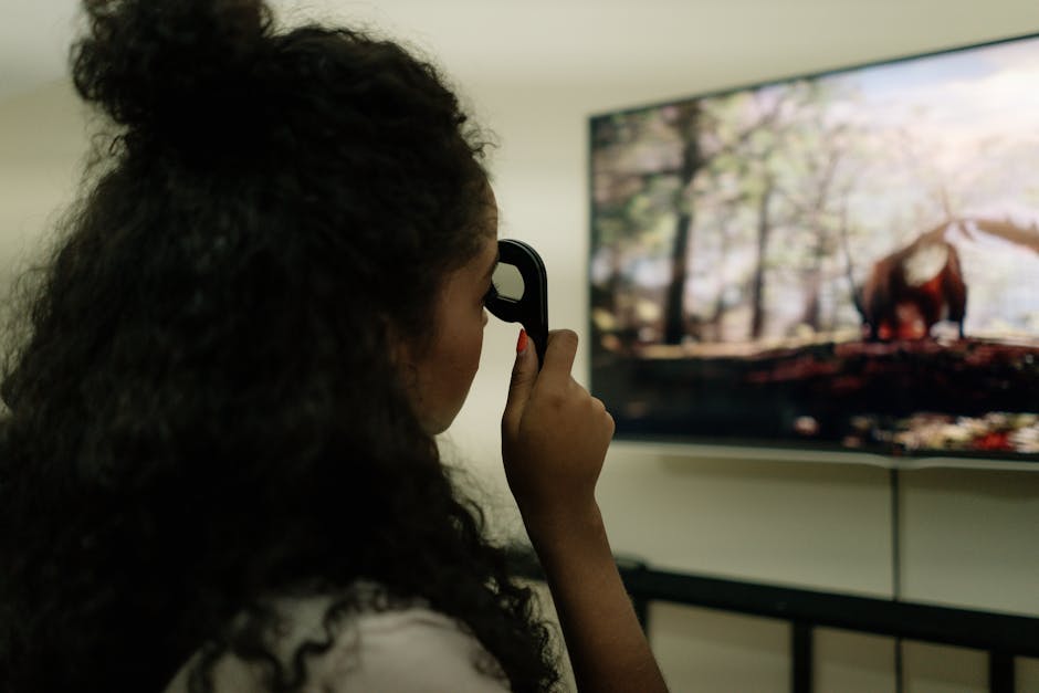 A woman with curly hair using a remote control to watch a nature documentary on a flat-screen TV indoors.