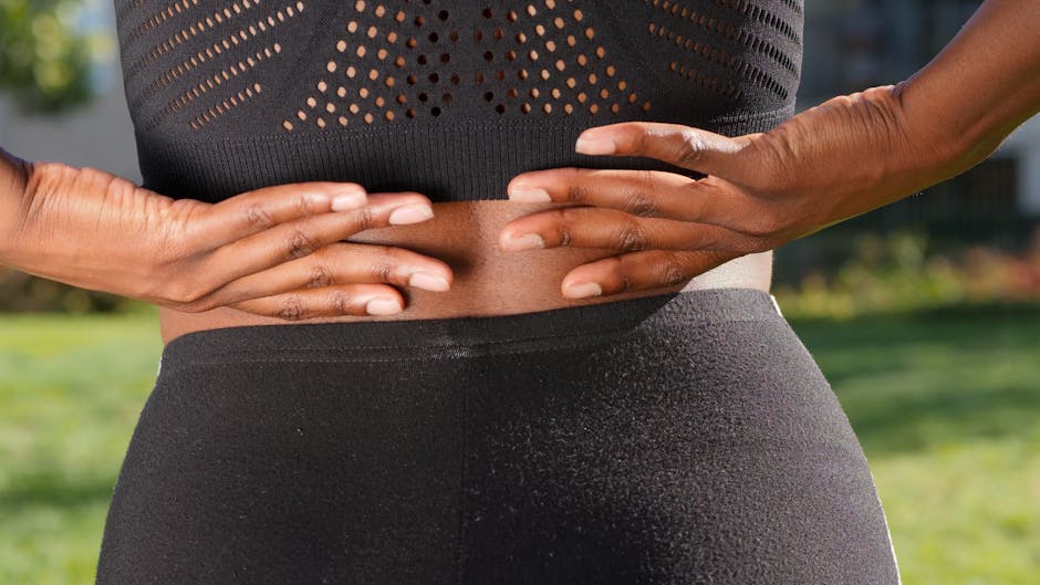 Close-up of a woman's hands gripping her painful back while outdoors.