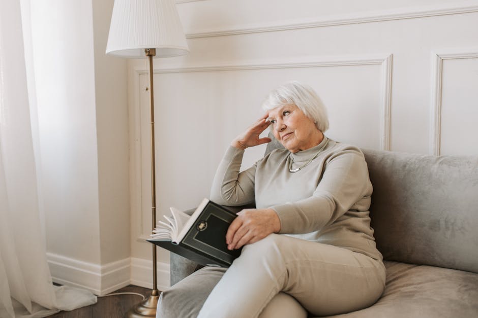 Senior woman sitting on a couch reading a book, with a thoughtful expression.