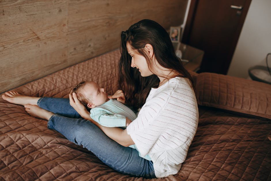 A young mother joyfully interacts with her baby on a bed in a cozy bedroom setting.