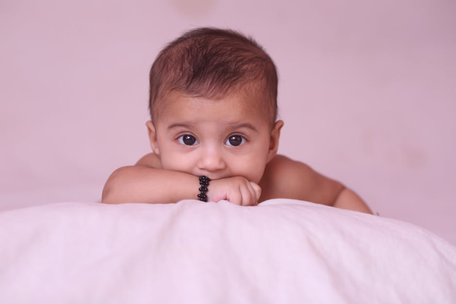 Cute baby with a bracelet lying on a white bed, looking curiously.