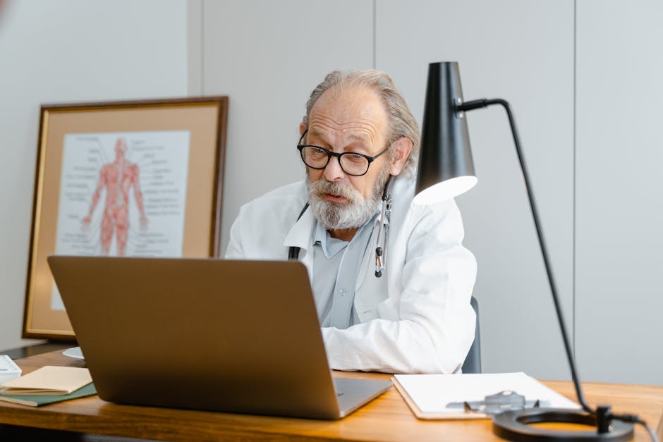 Senior doctor in a lab coat conducting a virtual consultation using a laptop in an office setting.