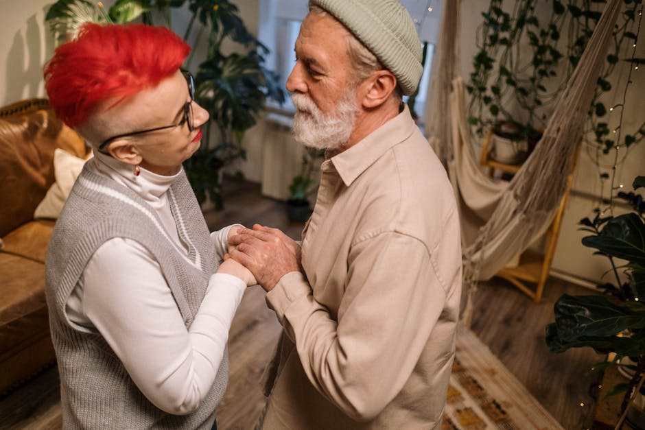 An elderly couple with red and grey hair, sharing an intimate moment indoors, holding hands lovingly.