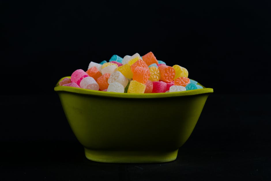 Vibrant gummy candies in a green bowl against a dark backdrop, capturing indulgent sweetness.