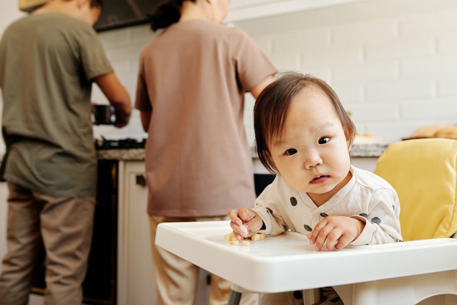 Cute toddler in a polka dot outfit sitting in high chair while parents cook in kitchen.
