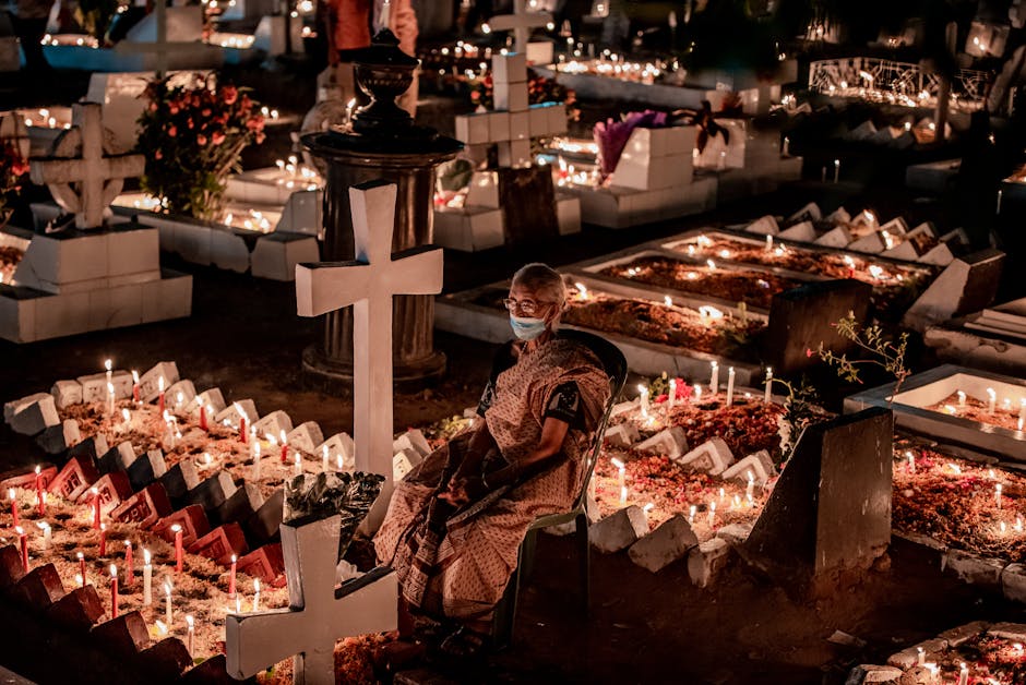 A person sits by a candlelit grave in a serene nighttime cemetery setting.