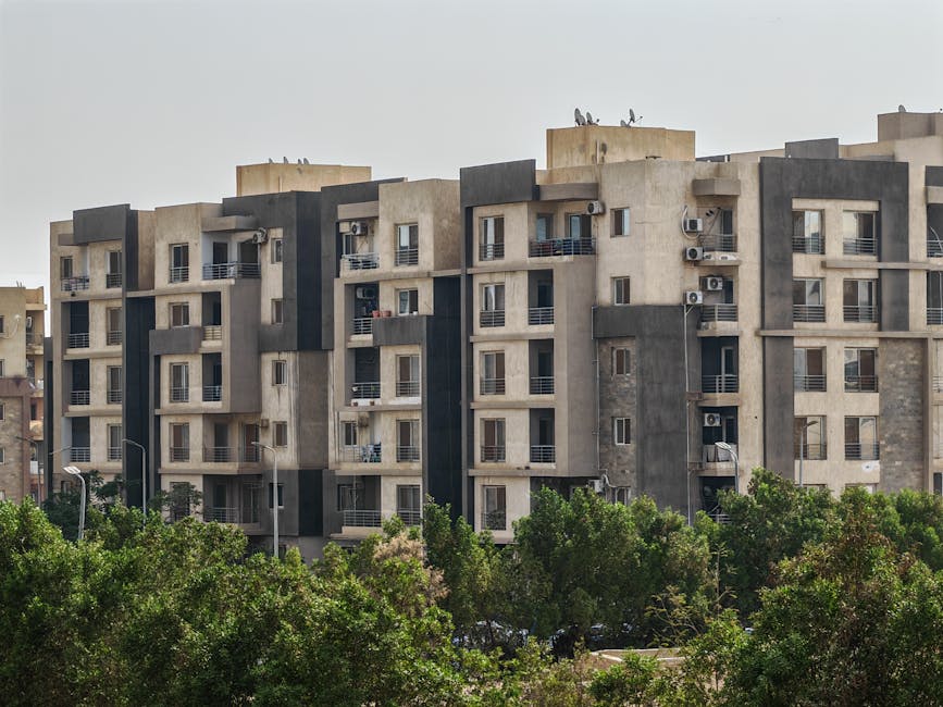 Urban residential apartment complex with trees in foreground on a clear day.