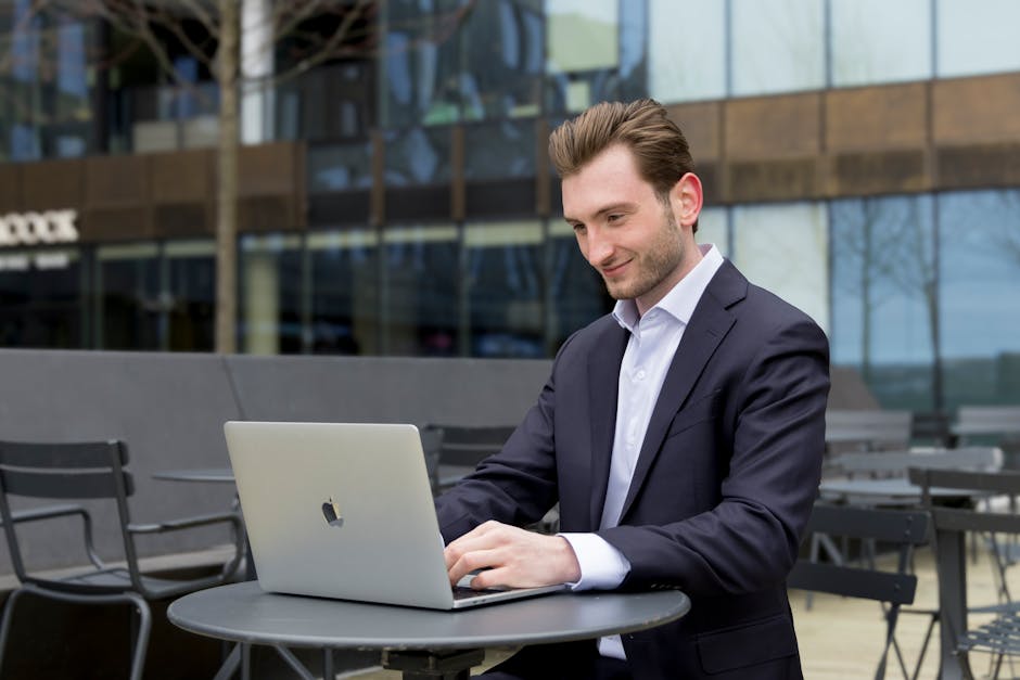 Caucasian man in suit using laptop outside modern building for work.