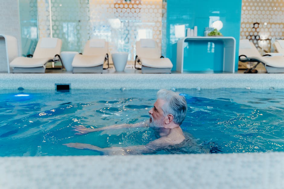 Older man enjoying a swim in a stylish indoor pool facility with relaxation chairs.