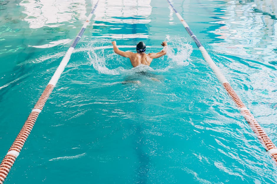 A male athlete swimming the butterfly stroke in a clear blue swimming pool, focusing on exercise and speed.