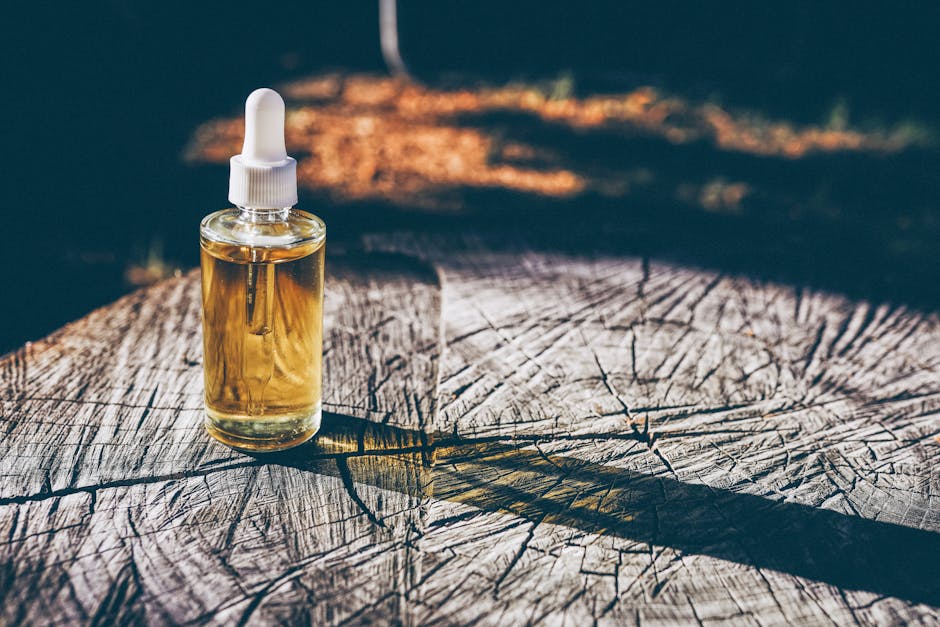 A glass dropper bottle with liquid placed on a textured wooden surface, outdoors in natural light.