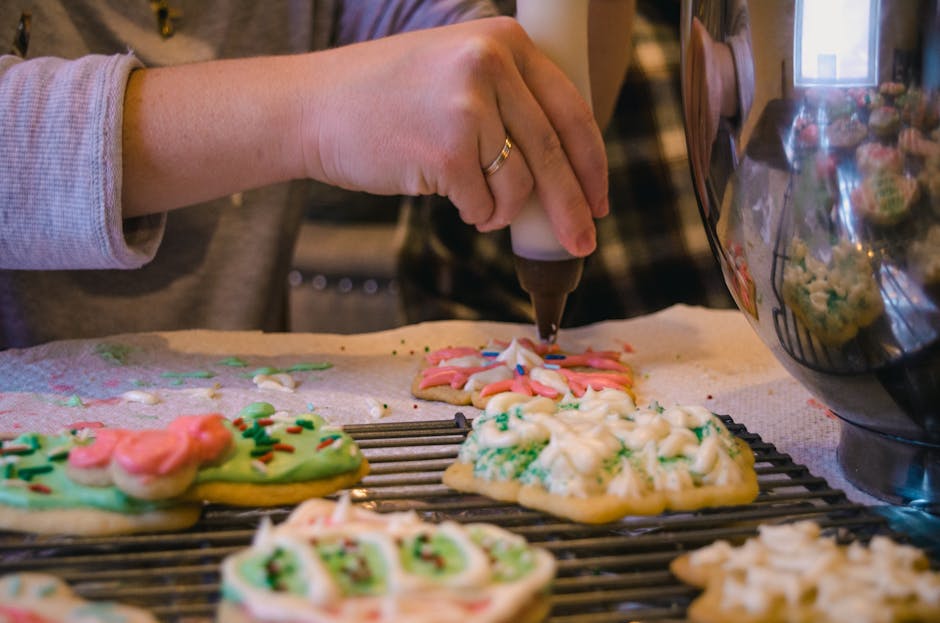 Person decorating Christmas cookies with icing and sprinkles indoors.