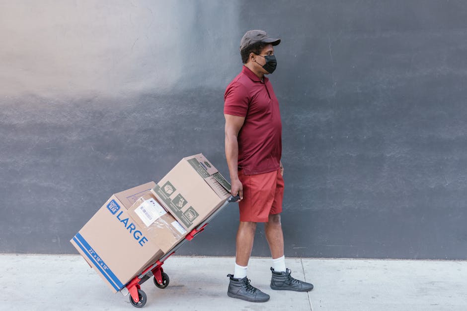 Man in protective mask pulling a trolley with boxes outside, highlighting safe delivery practices.