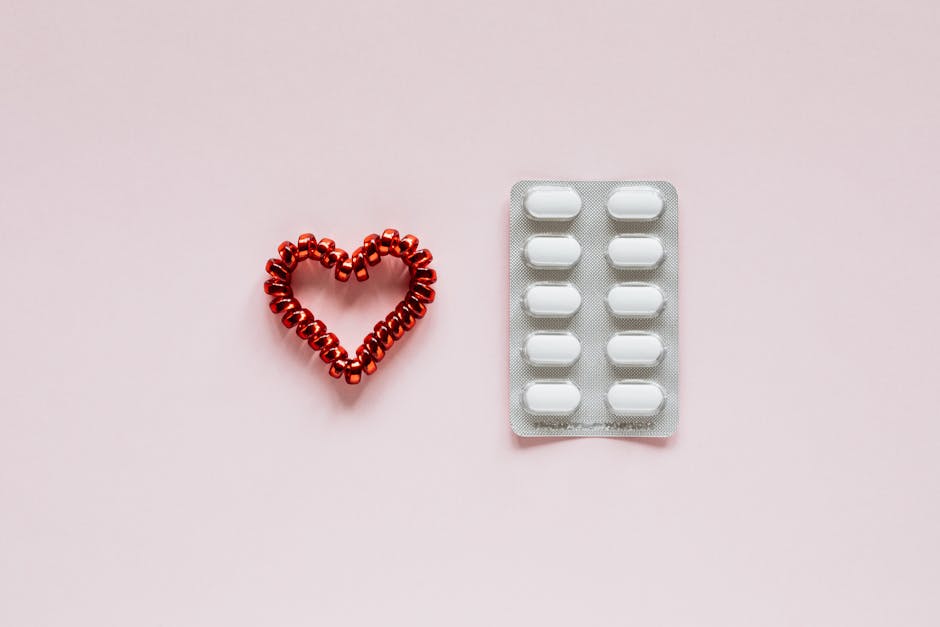 Top view of plastic blister with pills placed near red heart made of hair scrunchy on pink background
