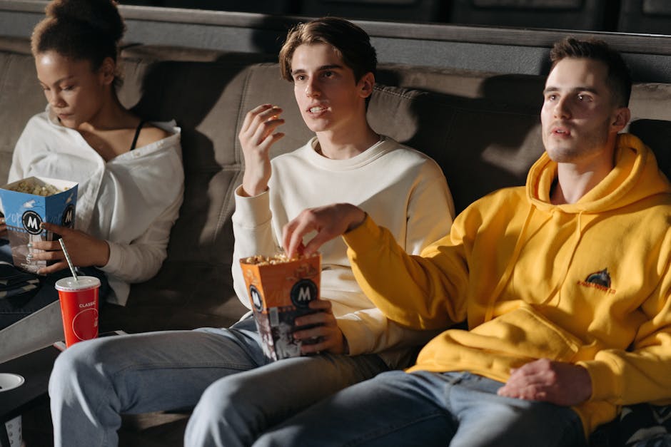 Three friends watching a movie indoors with popcorn and drinks, enjoying a relaxed evening together.