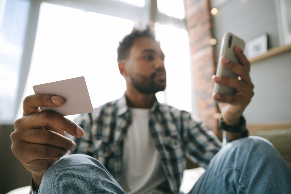 A man using a smartphone and card for online shopping in a cozy indoor setting.